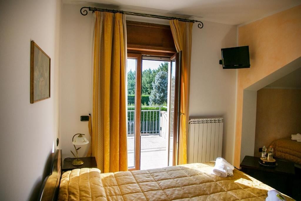 Habitación de hotel con cama, televisor montado en la pared y balcón con cortinas.