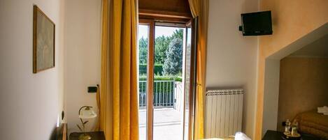 A hotel room with a bed, a television mounted on the wall, and a balcony with curtains.