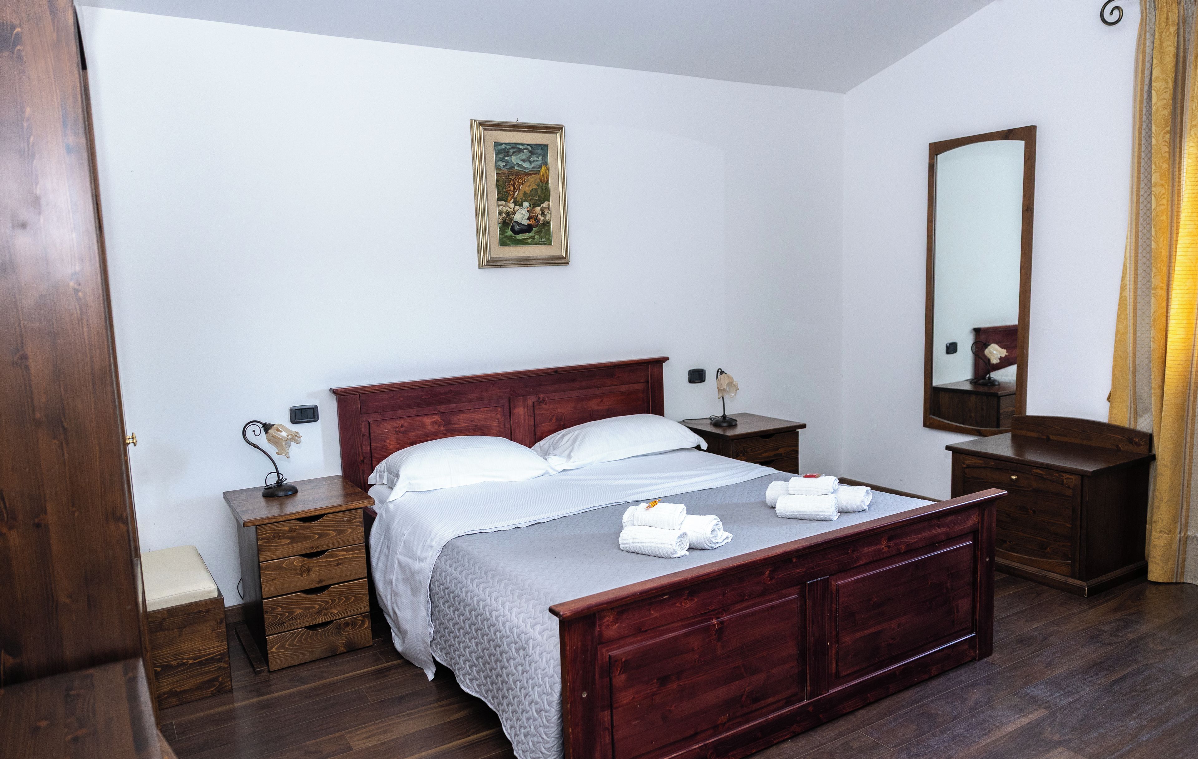 Un dormitorio con cama de madera, mesita de noche, espejo y un cuadro en la pared.
