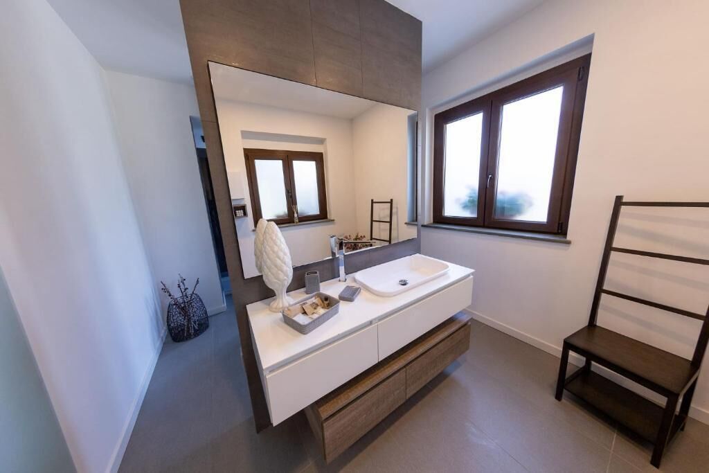 A modern bathroom with a large mirror, a white sink, and a wooden chair.