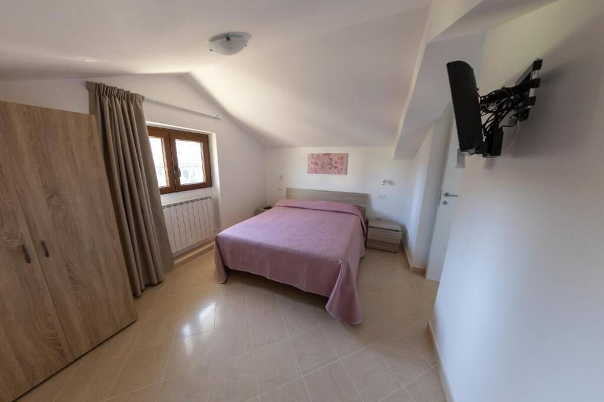A bedroom with a bed, a window, a wardrobe, and a wall-mounted TV.