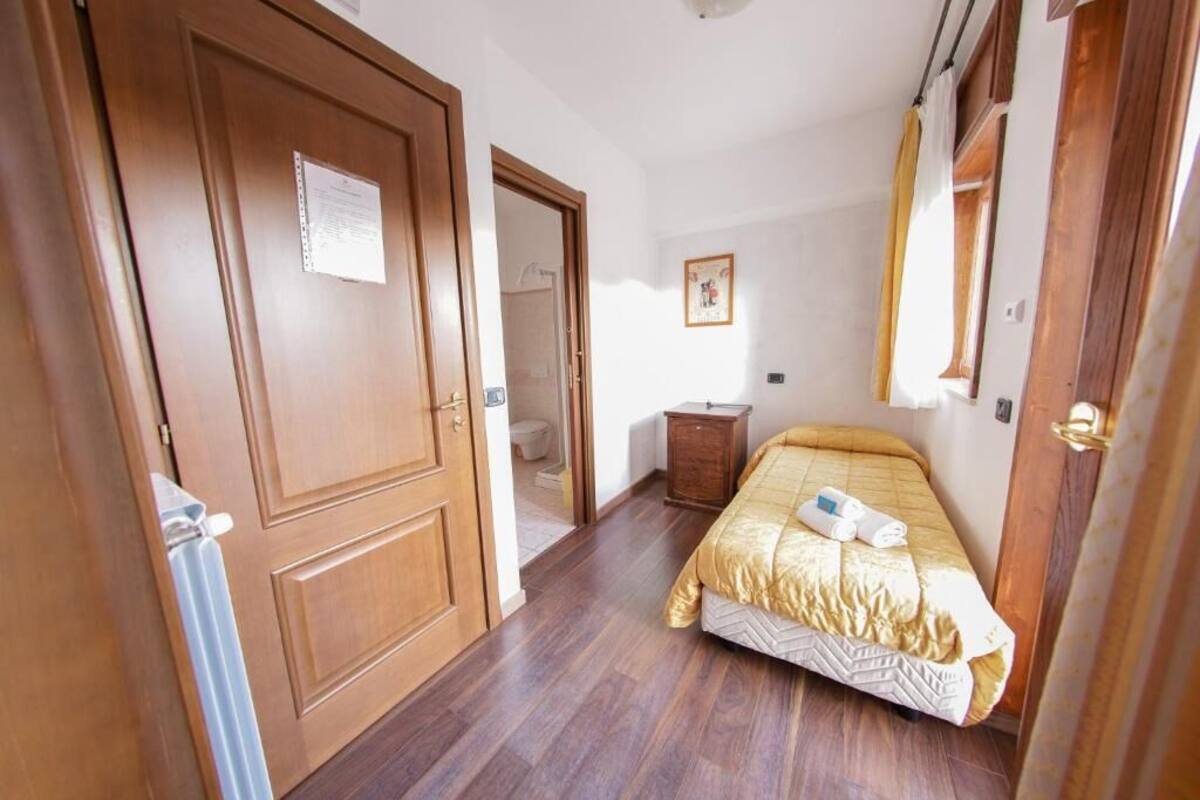 A hotel room with a bed, a wooden wardrobe, a small table, and a mirror.