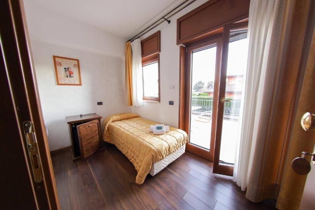 A bedroom with a bed, a small wooden dresser, a window, and a door.