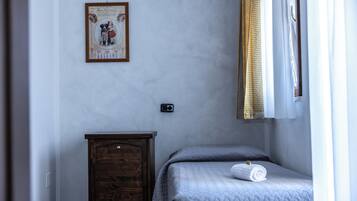 Une chambre à coucher avec un lit, une petite commode en bois, un interrupteur fixé au mur et un tableau encadré accroché au mur.