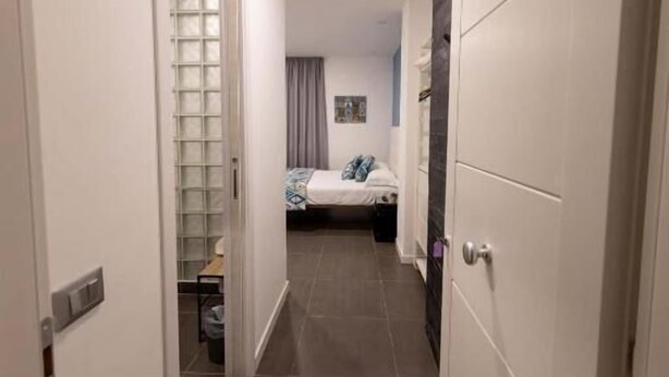 Um corredor estreito com uma cama ao fundo, uma porta à esquerda e outra à direita.