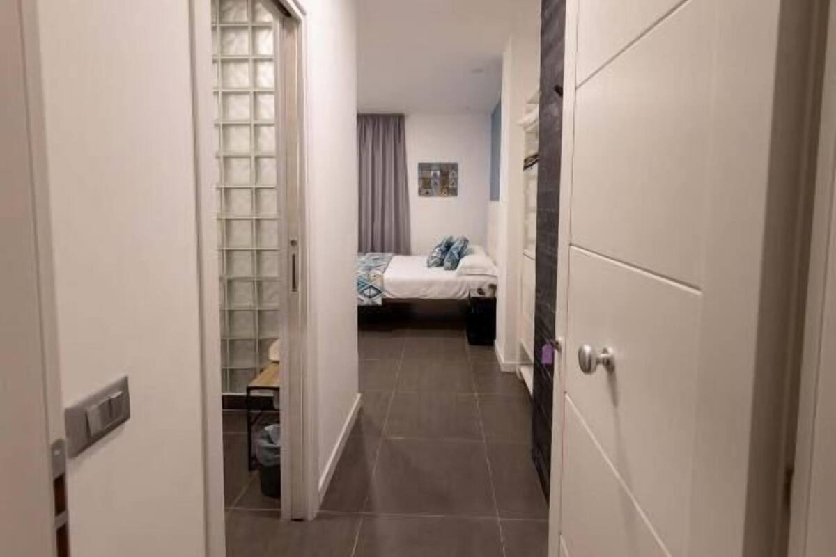 A narrow hallway with a bed in the background, a door on the left, and a door on the right.