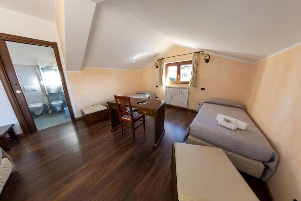 A small, cozy room with a bed, a desk, and a chair. There is a window with curtains and a view of the outside.