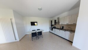 Cozinha moderna com armários brancos, uma mesa de jantar com cadeiras e uma televisão de tela plana fixada na parede.