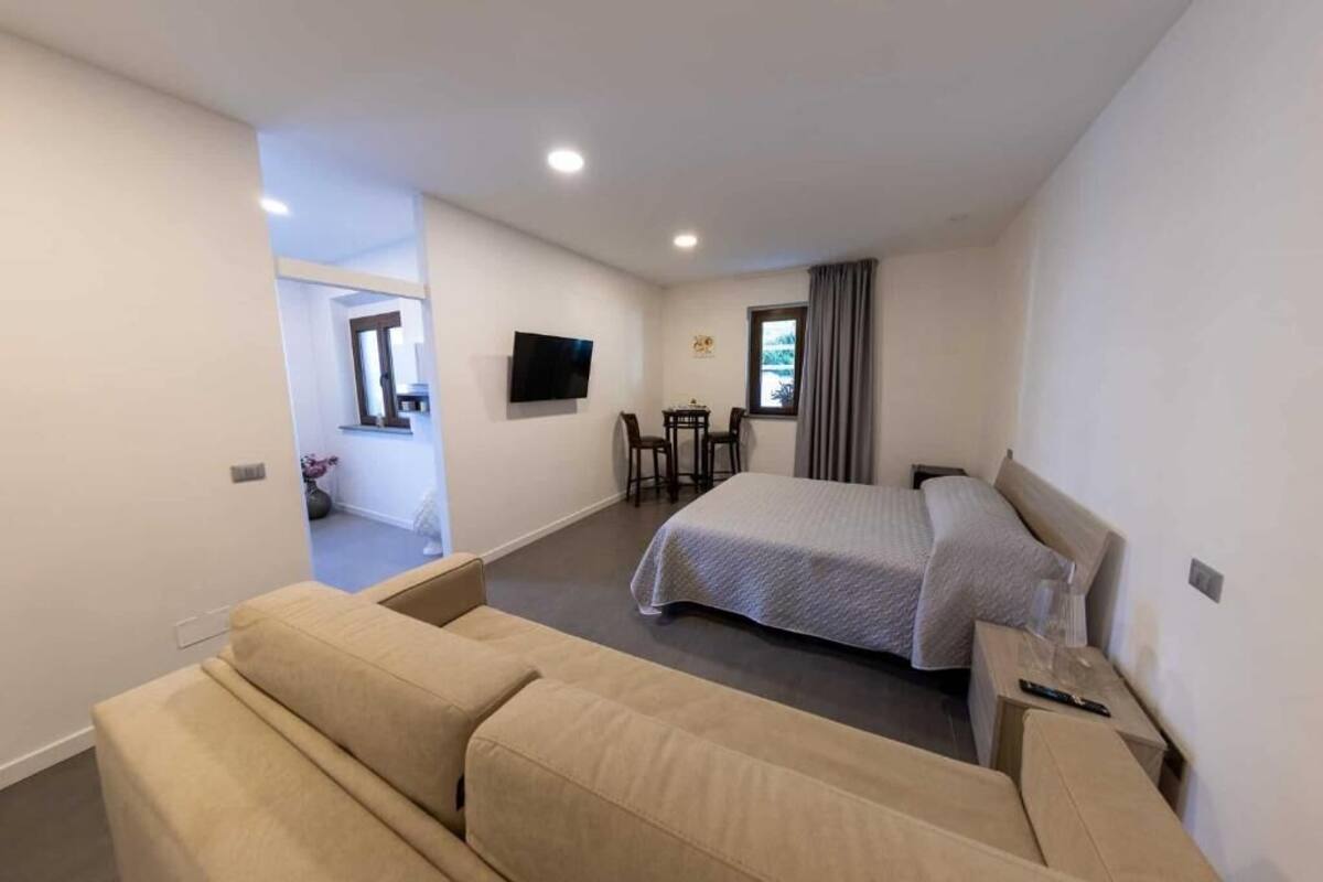 A hotel room with a bed, a sofa, a TV, a window with curtains, and a small table.
