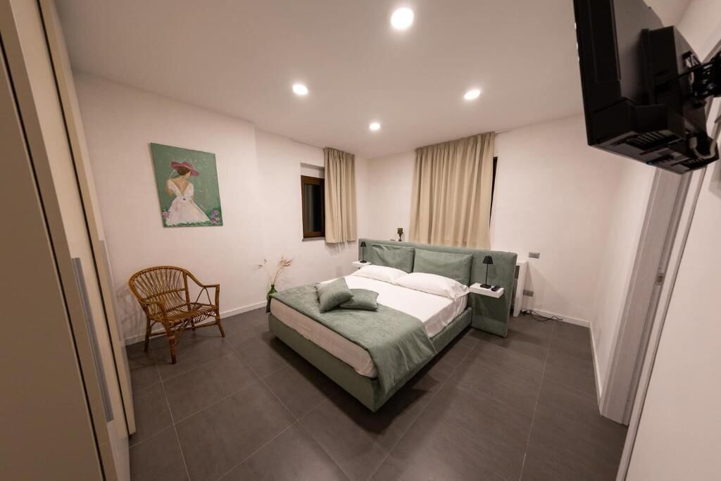 A bedroom with a bed, a chair, a painting, and a television.