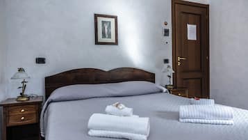 Ein Hotelzimmer mit einem hölzernen Kopfende, einem Bett mit grauer Decke, zwei Nachttischlampen, einem Nachttisch, einer Tür mit einem Schild und einem gerahmten Bild an der Wand.