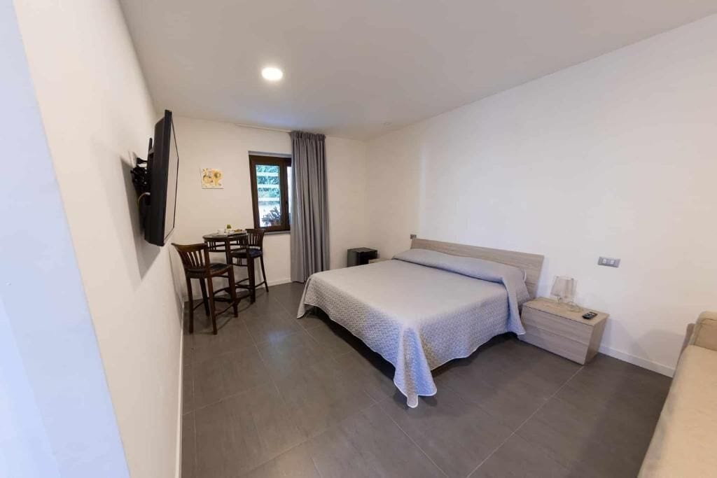 Un dormitorio con cama, escritorio, silla, televisor y ventana.