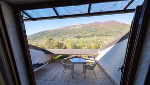 Uma varanda com mesa e cadeiras, vista para uma paisagem montanhosa e céu claro.