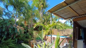 Un jardín tropical con piscina, cerca de madera y una casa moderna con porche cubierto.