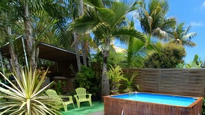 Un patio trasero con piscina, sillas verdes y una terraza de madera.