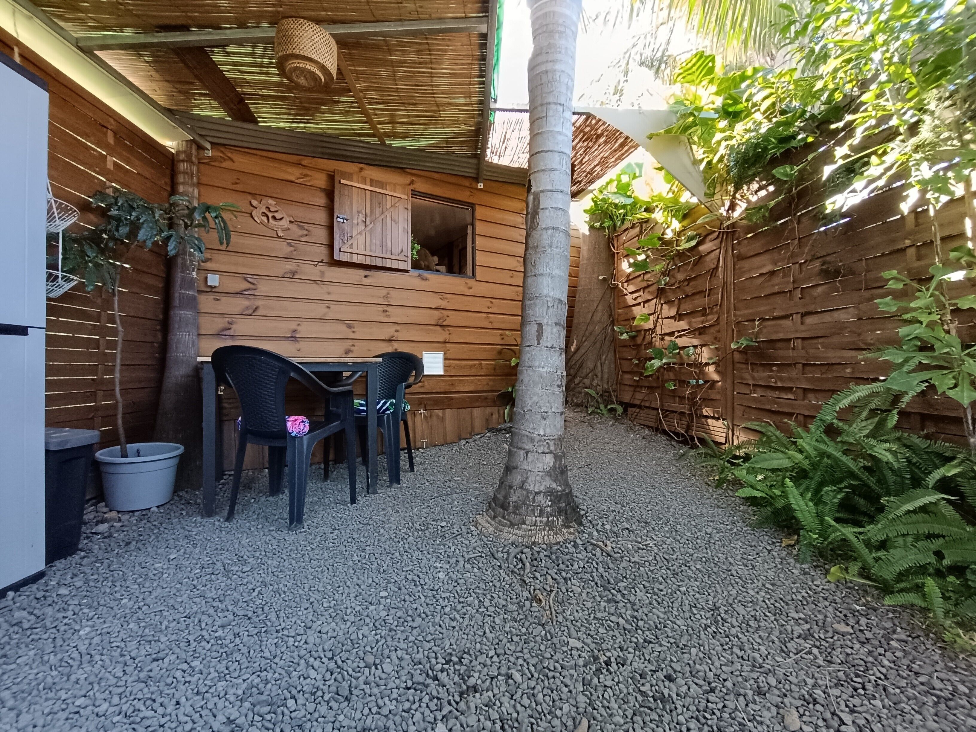 A wooden cabin with a gravel patio, a table with chairs, and a hanging basket.