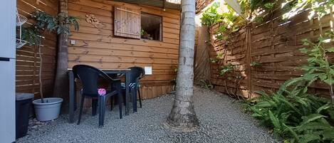 A wooden cabin with a gravel patio, a table with chairs, and a hanging basket.
