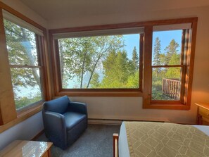 A room with a bed, a chair, and large windows with a view of trees and a deck. - Located directly on Lake Superior, this bright and comfortable condo is ideal for families or groups (Lutsen)