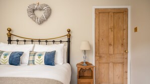 Un dormitorio con cama, almohadas, una mesita de noche, lámpara, puerta de madera y un adorno con forma de corazón en la pared.