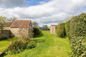 A garden with stone buildings, a grassy path, and various plants.