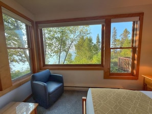 Une chambre avec un lit, une chaise et de grandes fenêtres donnant sur des arbres et une terrasse.
