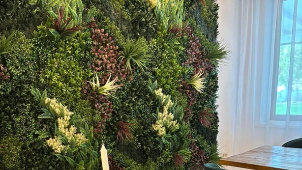 Uma mesa de madeira com diversos petiscos e uma vela, com um fundo de parede e uma planta verde.