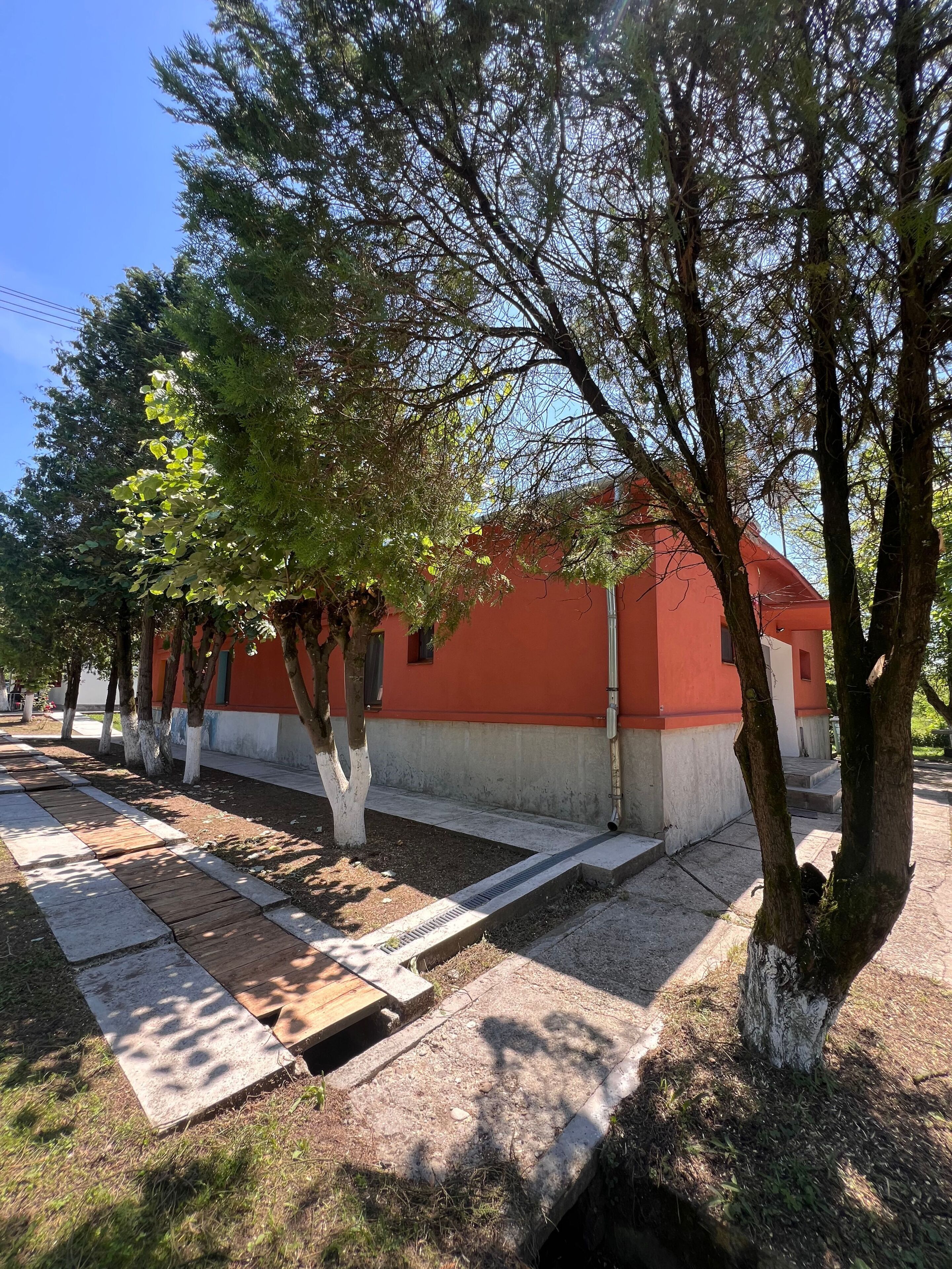 A building with a red facade, surrounded by trees and a paved walkway.