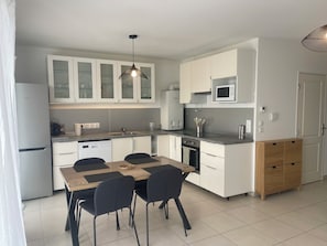 A modern kitchen with white cabinets, a dining table with chairs, a microwave, and a coffee machine. - Cosy apartment with terrace, private garage, near beach and port of Hyères (Hyères)