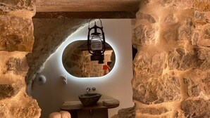 A rustic bathroom with a stone wall, a round mirror, a wooden basin, and a lantern.