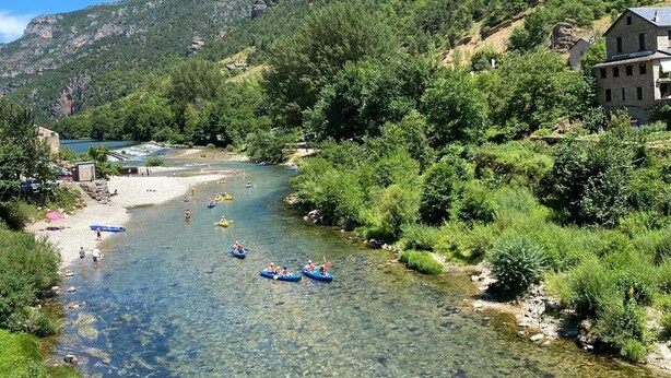 A clear river with people kayaking, surrounded by lush greenery and mountains.