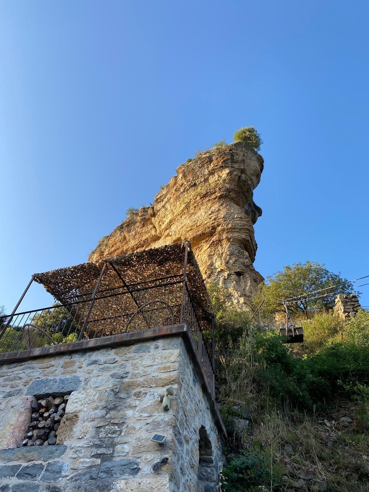 Una estructura de piedra con barandilla metálica y una formación rocosa al fondo.