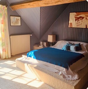 Ein Schlafzimmer mit Bett, Nachttisch, Lampe, Heizkörper und einem Fenster mit Vorhängen.