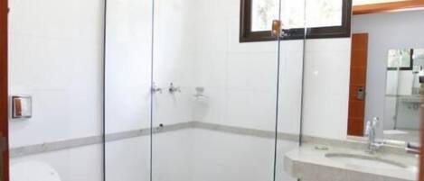 Un baño con ducha de vidrio, inodoro, lavamanos y espejo.