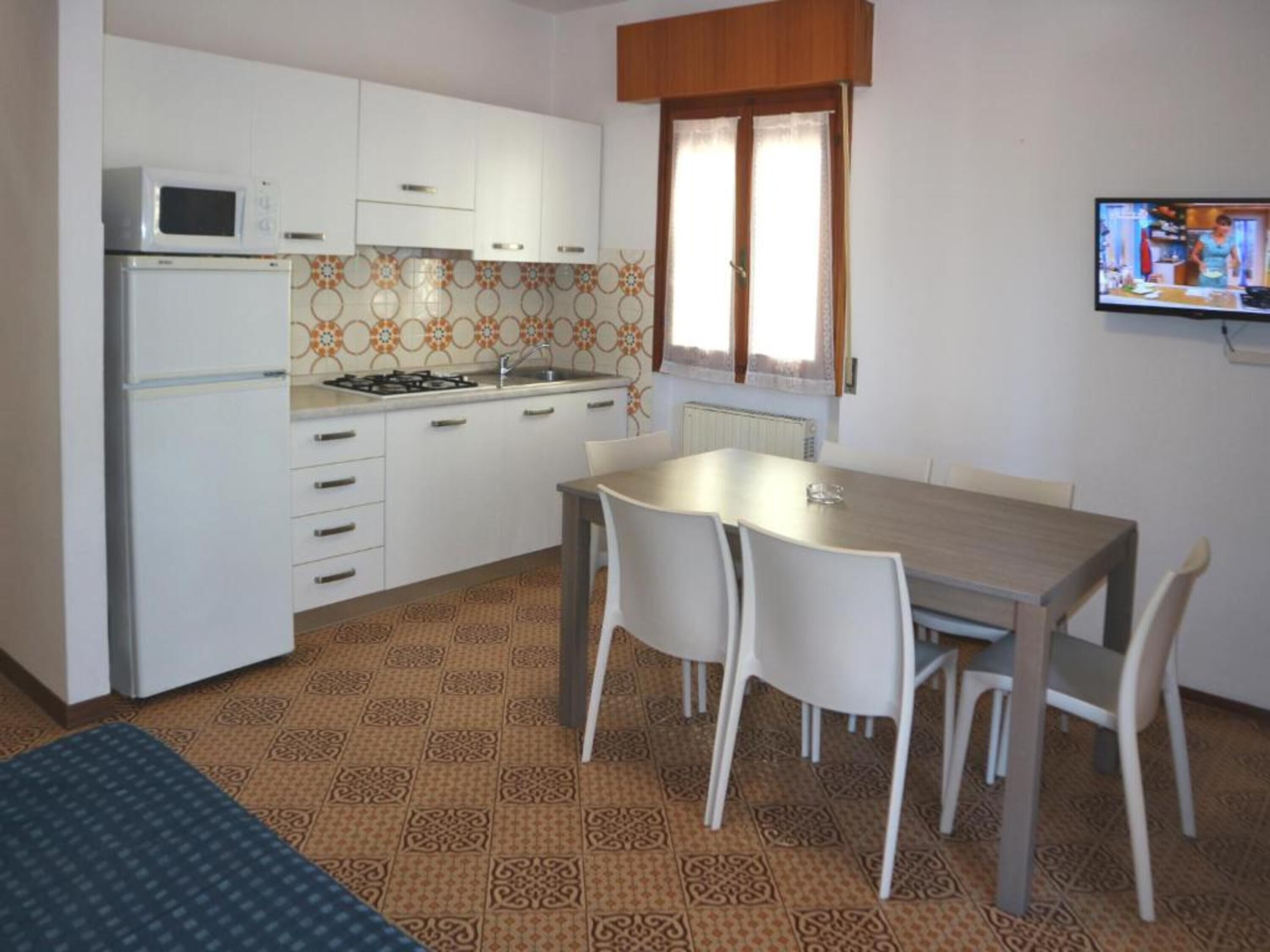 Uma cozinha compacta com armários brancos, micro-ondas, fogão e uma mesa de jantar com cadeiras.