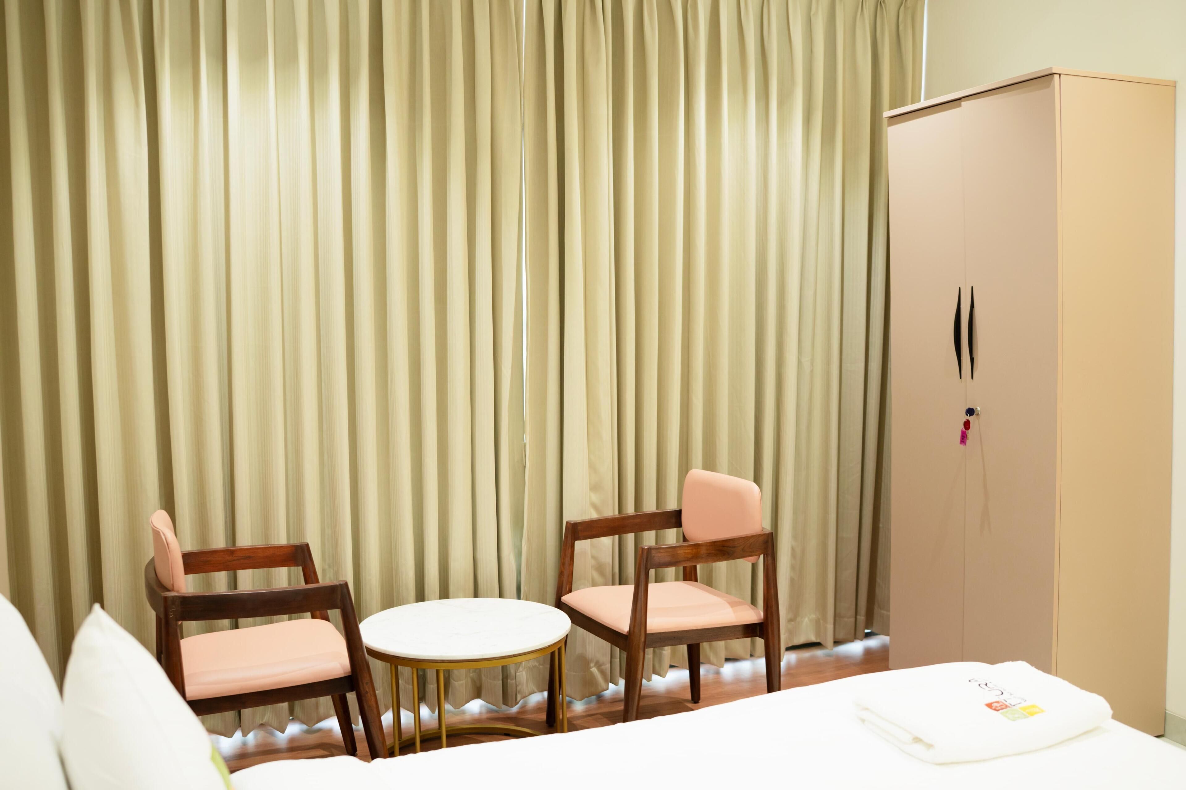 Una camera d'albergo con due sedie di legno, un tavolino rotondo, un armadio e un letto.