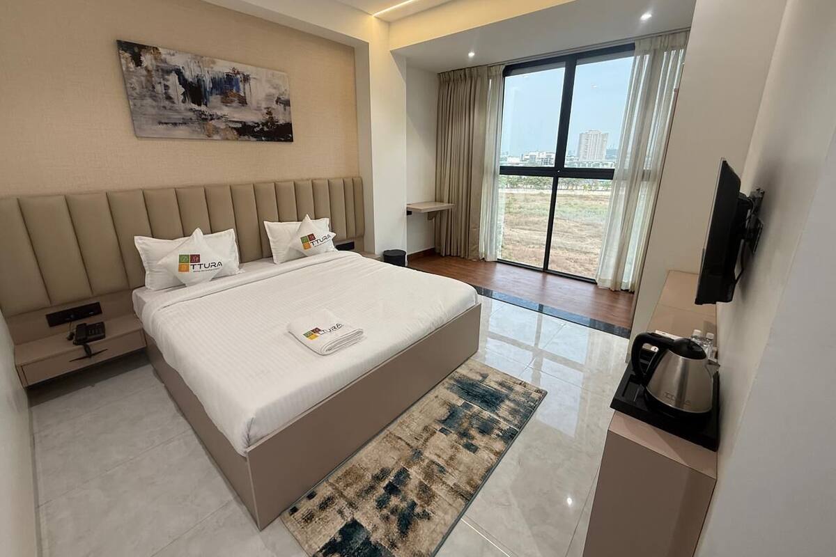 A modern hotel room with a large bed, a flat-screen TV, a coffee maker, and a view of the outdoors.