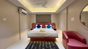 A bedroom with a bed, a red chair, a ceiling fan, and an air conditioning unit. - TTURA Kitchen Bar Rooftop & Rooms Pune  (Paud)