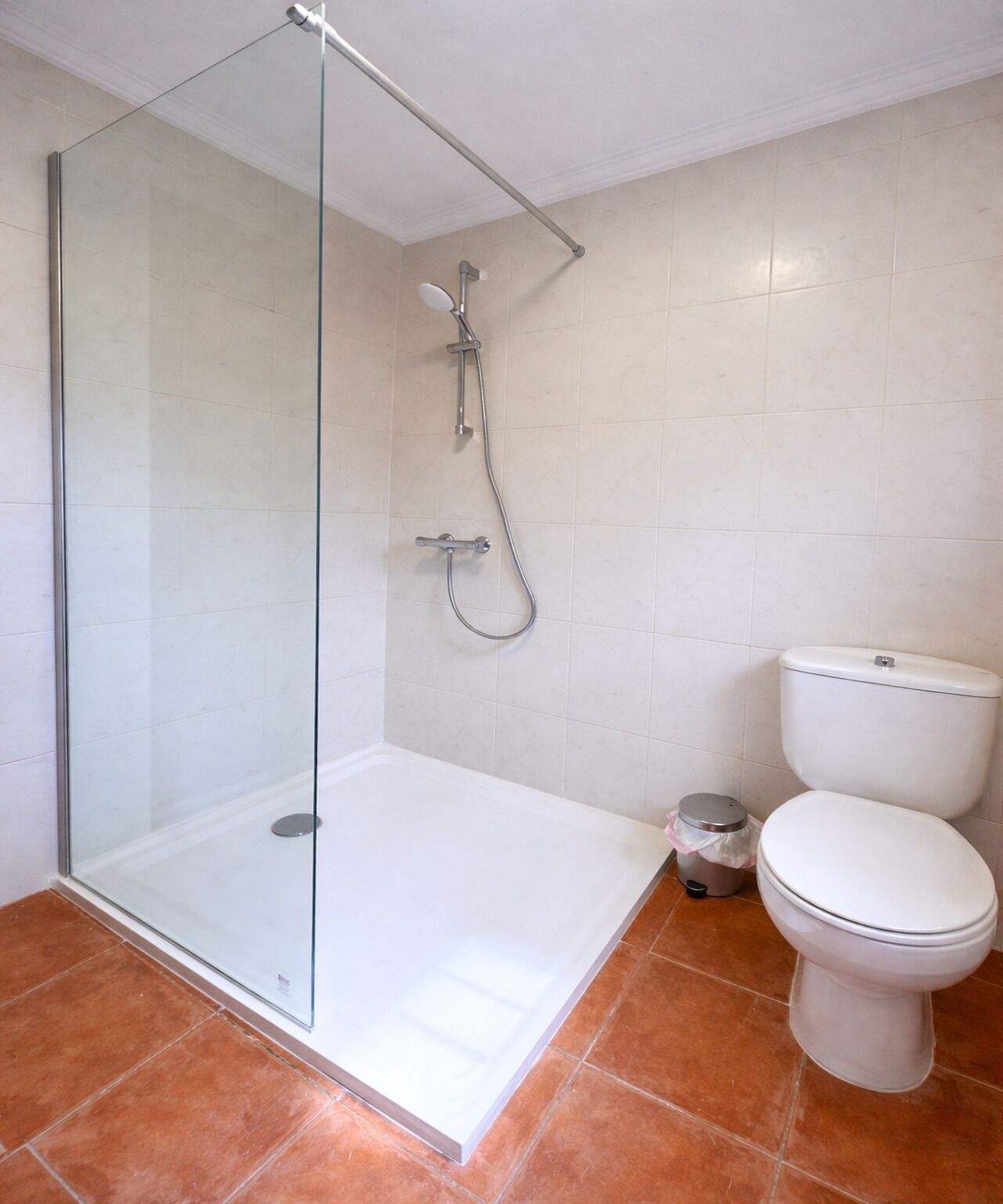 Un baño con ducha envuelta en vidrio, inodoro y un cubo de basura.