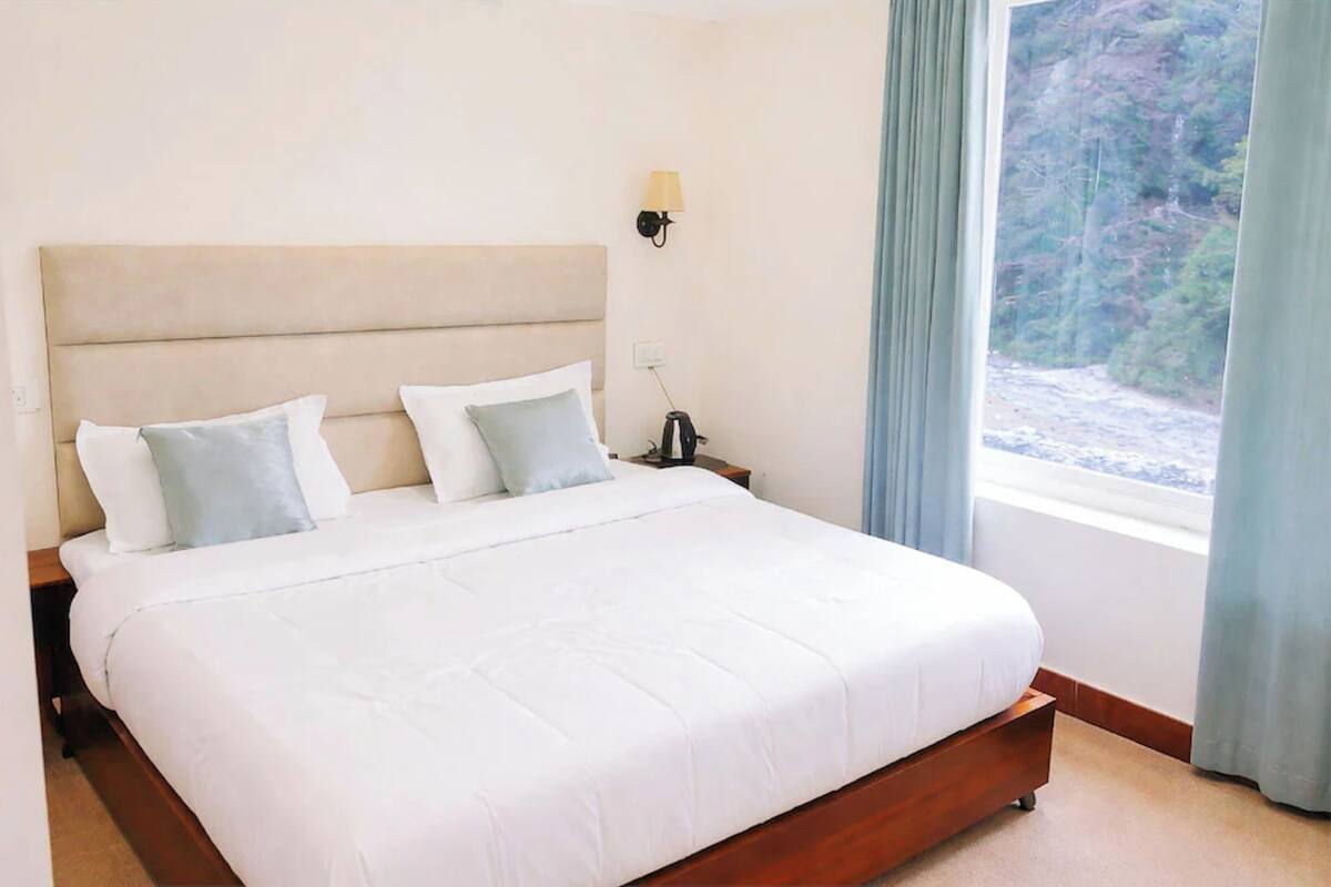 Una cama bien hecha con cabecera de madera, una lámpara de noche y una ventana con cortinas.