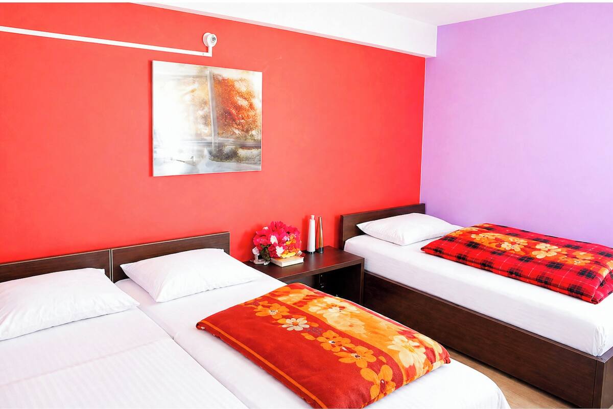 Habitación de hotel con dos camas, una mesita de noche con un jarrón de flores y un cuadro en la pared.