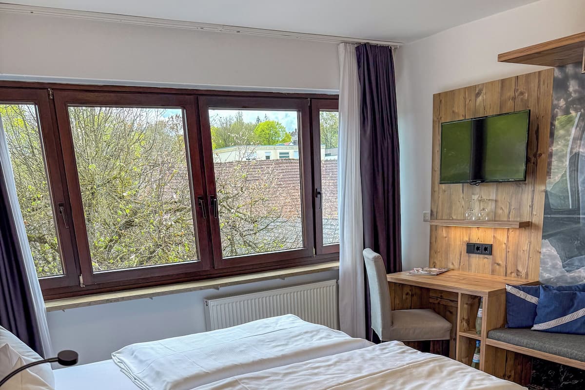Ein Hotelzimmer mit einem großen Bett, einem Schreibtisch, einem Sessel und einem an der Wand befestigten Fernseher.