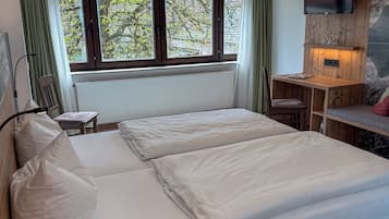 Une chambre à coucher avec un lit, un bureau, une chaise, une télévision et une fenêtre avec des rideaux.