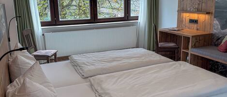 A bedroom with a bed, a desk, a chair, a TV, and a window with curtains.