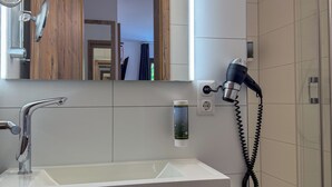 A modern bathroom with a large mirror, a sink, a hairdryer, and a shower. - Hotel-Restaurant Dechbettener Hof (Regensburg)