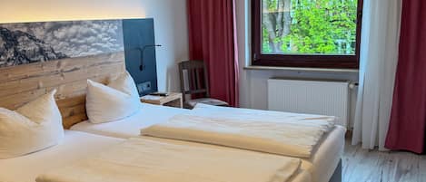 A hotel room with a large bed, a desk, a chair, a window with a view of trees, and a ceiling light.