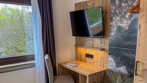 A room with a wooden desk, a chair, a TV mounted on a wooden wall, a sofa, and a radiator. - Hotel-Restaurant Dechbettener Hof (Regensburg)