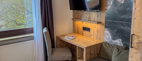 Et værelse med et træskrivebord, en stol, et TV ophængt på en trævæg, en sofa og en radiator.