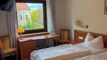 A hotel room with a bed, a desk, a chair, a TV, and a window with a view of a building.