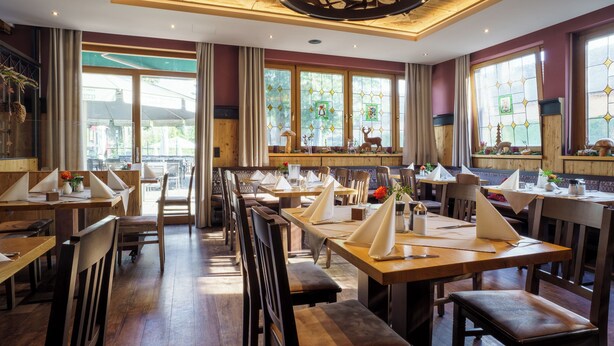 A restaurant with wooden tables and chairs, large windows with decorative glass, and a wooden ceiling with a circular light fixture. - Hotel-Restaurant Dechbettener Hof (Regensburg)