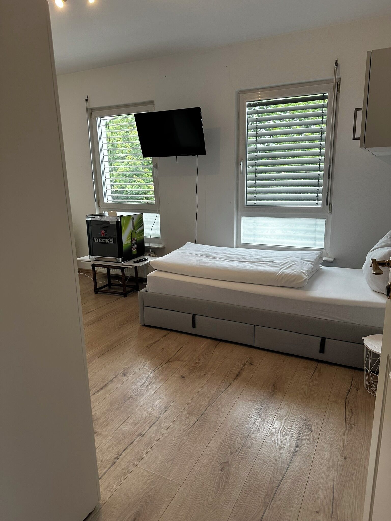 A bedroom with a bed, a TV mounted on the wall, and a window with blinds.